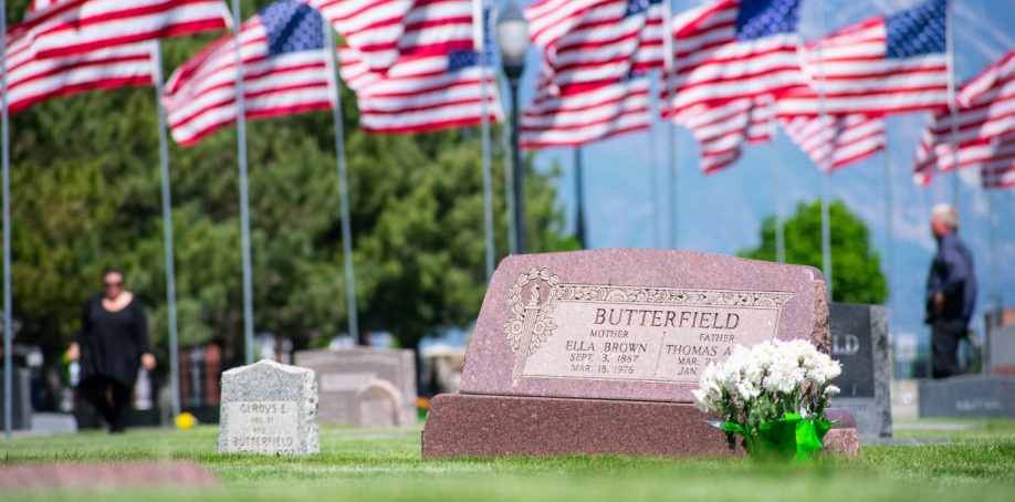 A headstone at the Herriman City Cemetery with a series of American flags shown in the background.