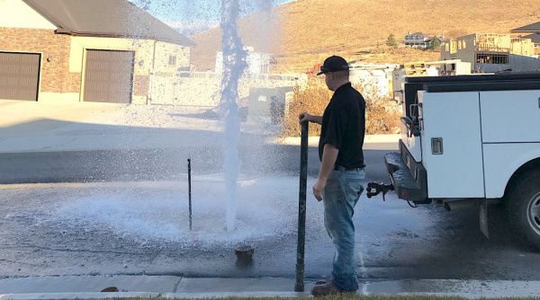 Water gushes out of an opening in the road as a City employee watches the flushing process